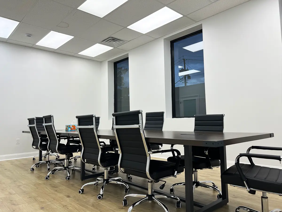 A professional conference room setup with sleek black leather chairs and a long wooden table under bright ceiling lights.