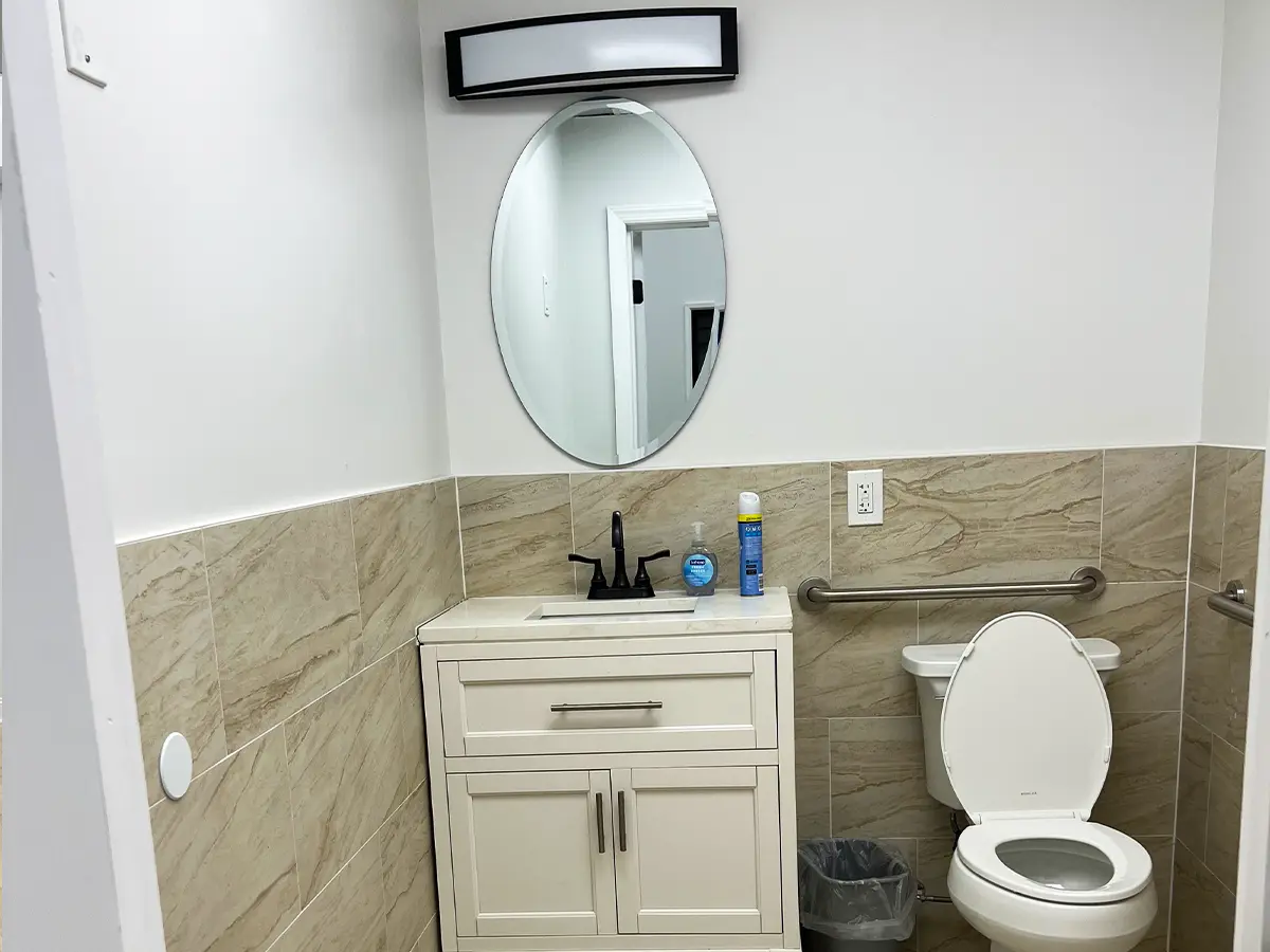A restroom featuring a simple design with a white vanity, oval mirror, and tiled walls.