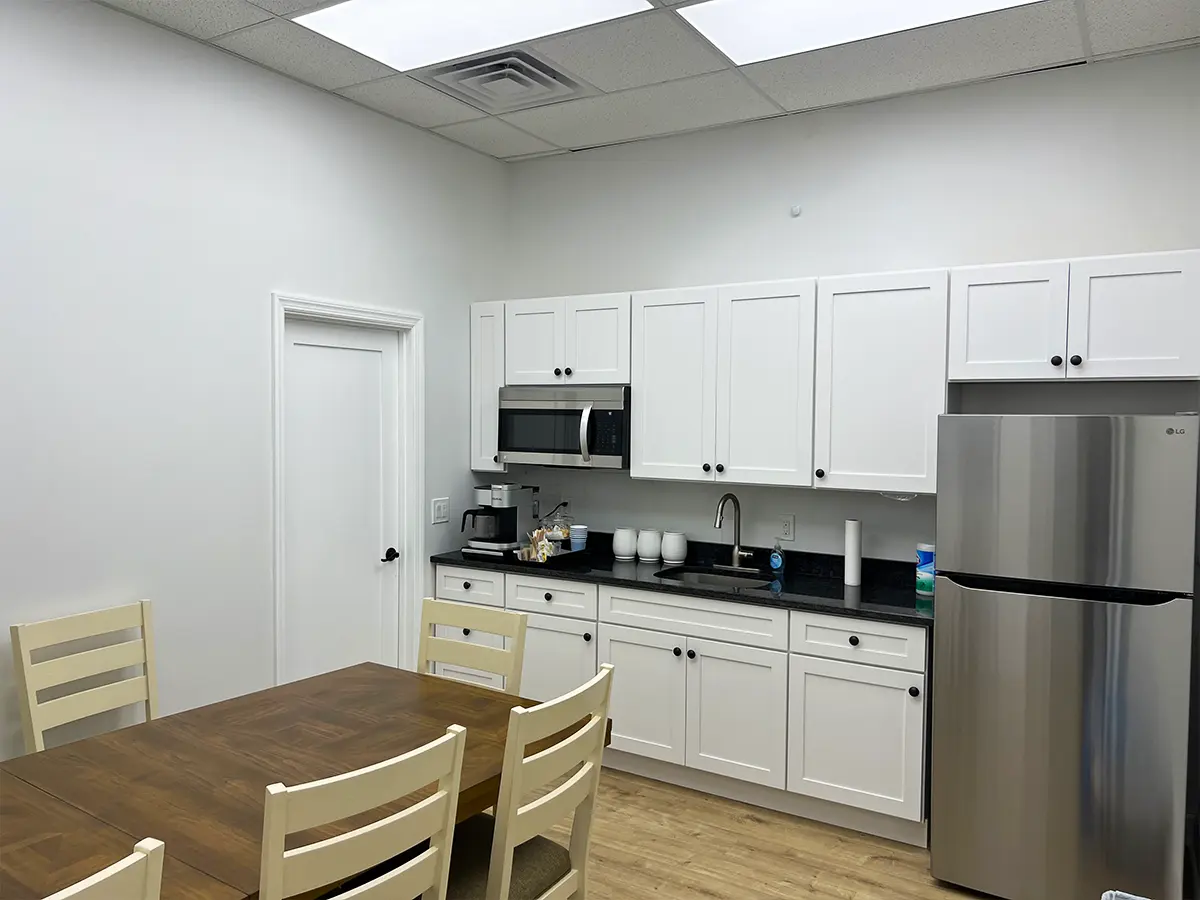 A small office kitchen with a table and chairs, white cabinets, a stainless steel refrigerator, and a microwave for employees.