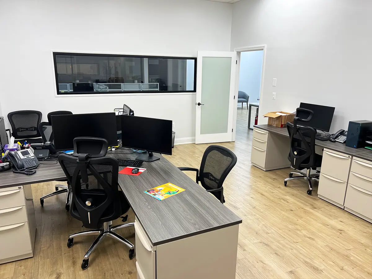 A modern office setup with ergonomic chairs, wooden desks, and computer monitors in an open workspace design.
