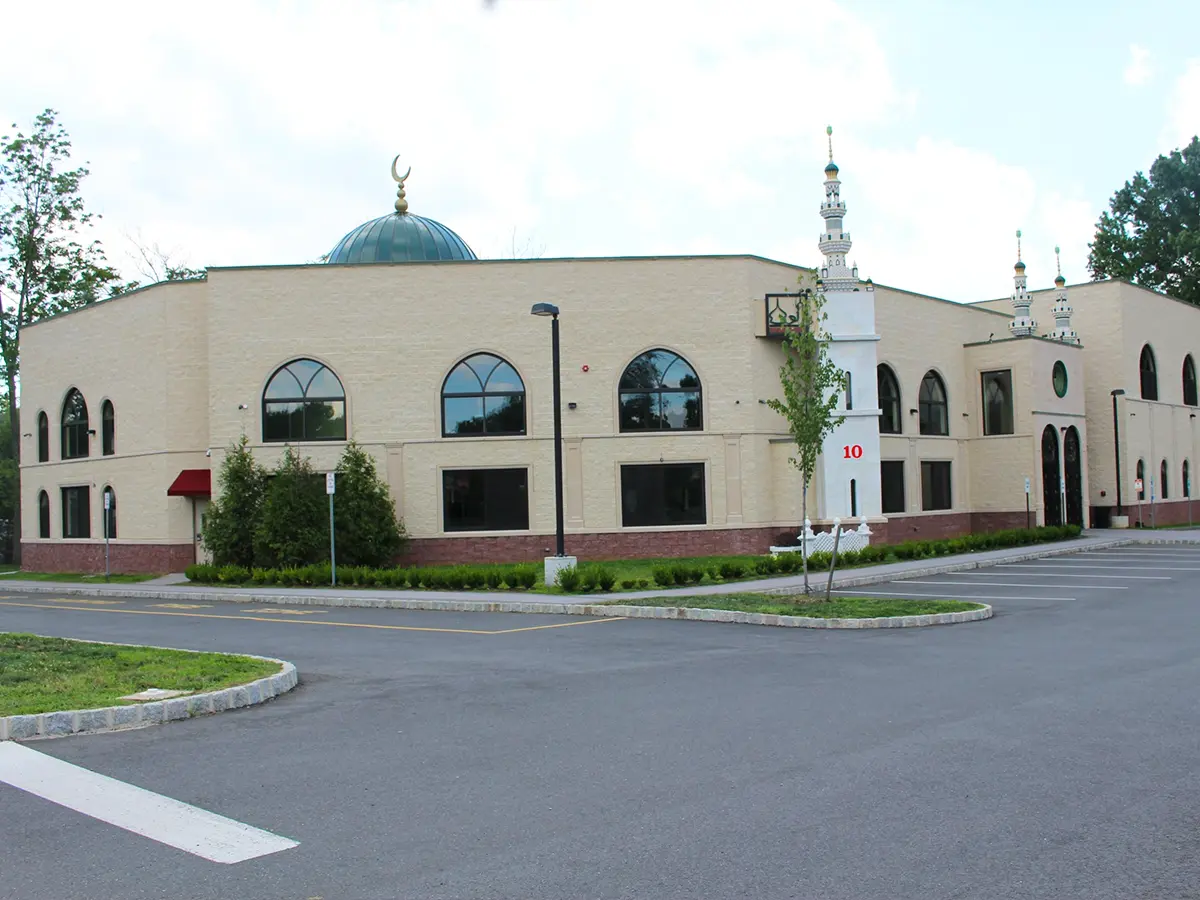 Exterior of Al-Wali Center mosque with domed roof and minarets, featuring a landscaped parking lot.