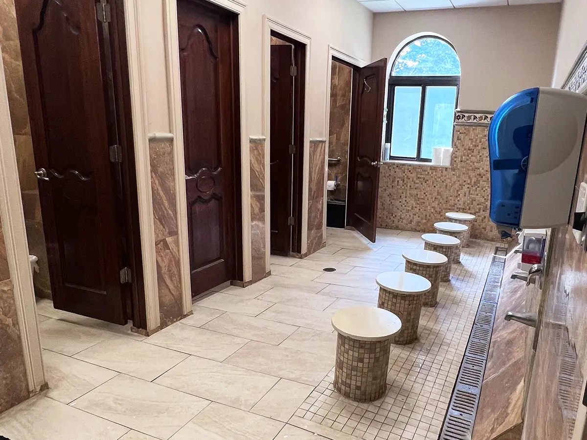 Marble-tiled mosque restroom with wudu area and wooden doors at Al-Wali Center.