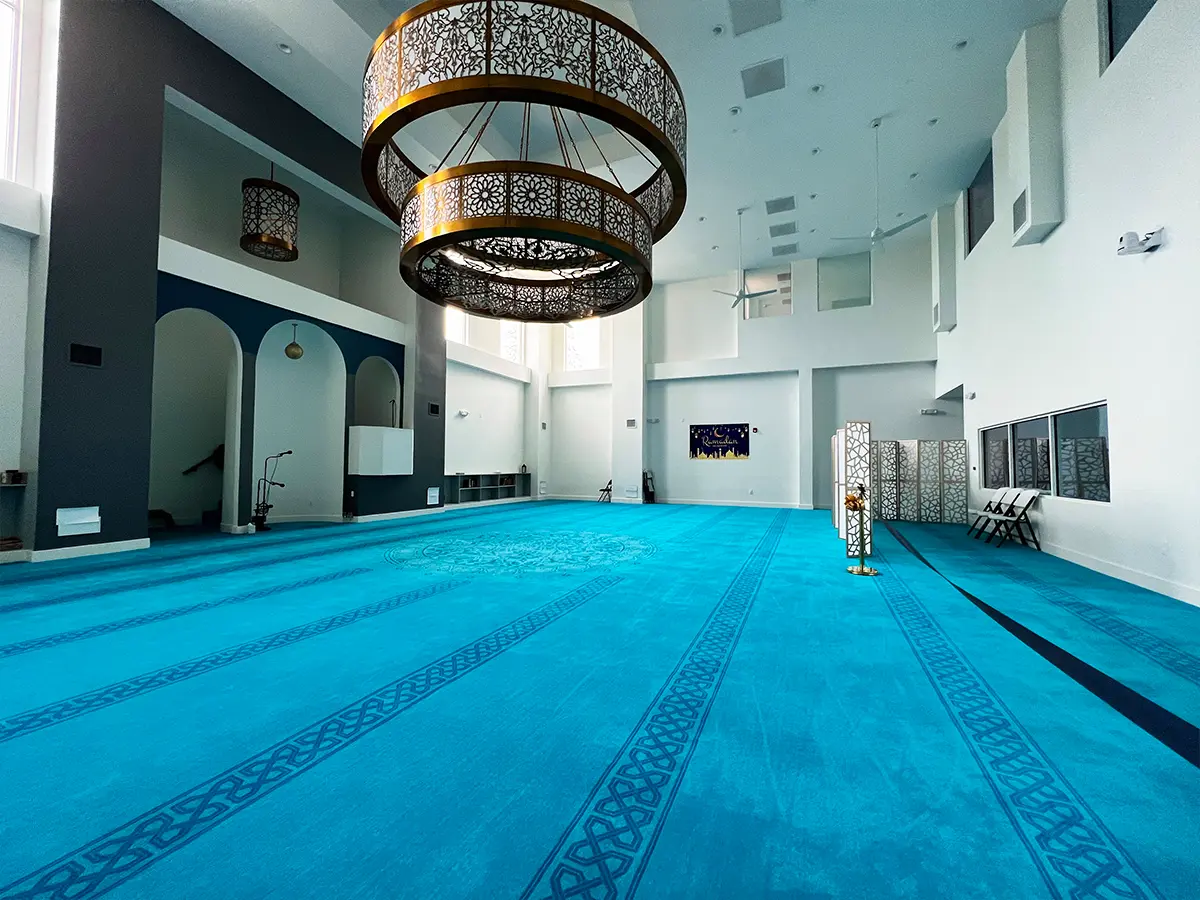 Spacious mosque interior with decorative chandeliers and blue prayer carpets - Presenting a well-lit mosque hall designed for large congregations.