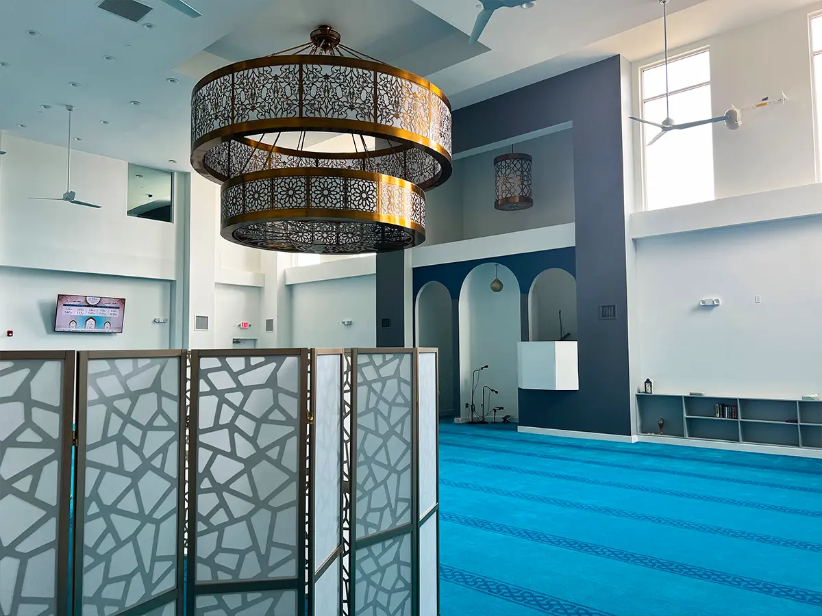 Modern mosque prayer area with intricate chandeliers and blue carpeting