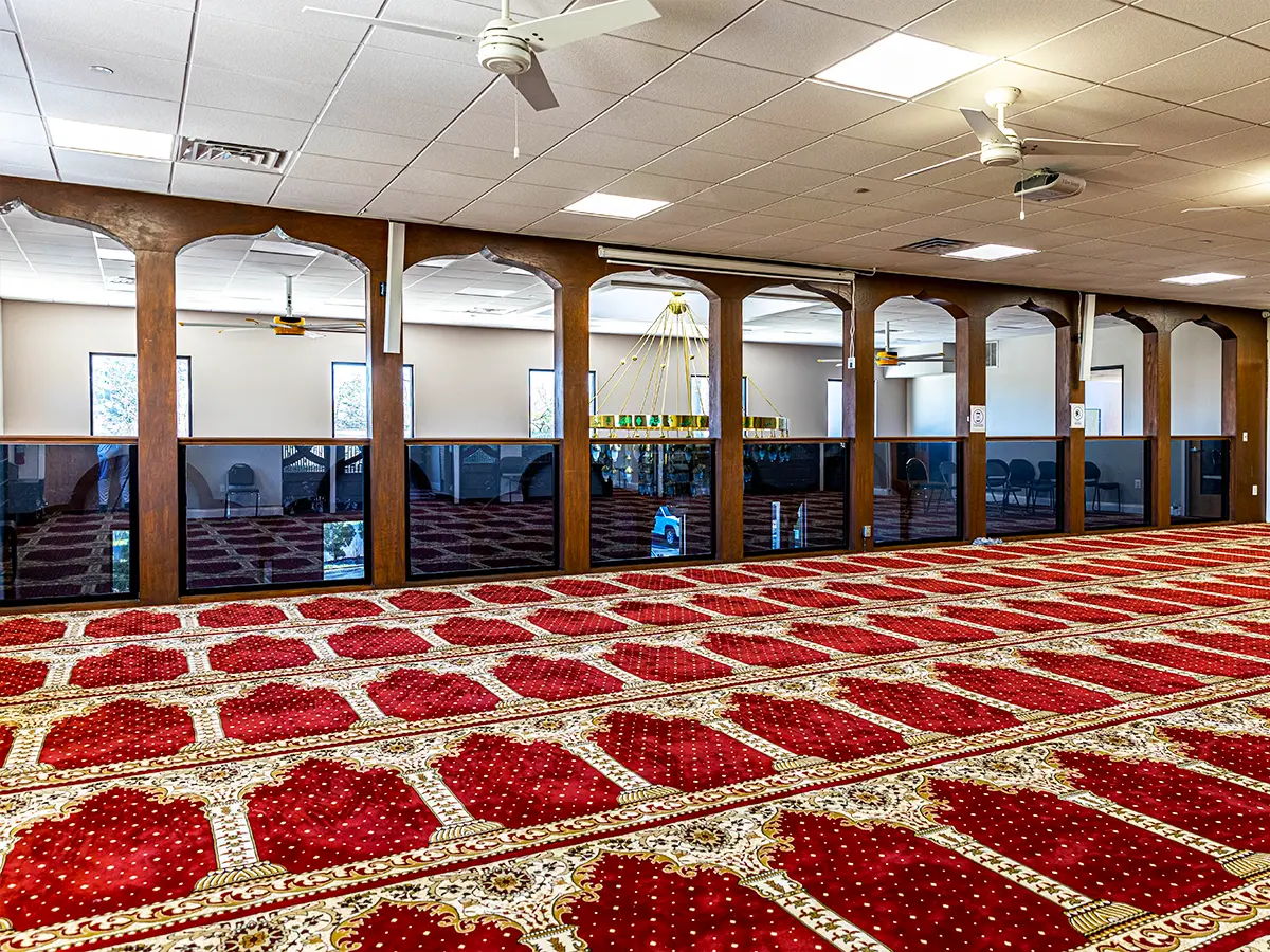 Spacious prayer hall with red carpet, arched wood dividers, and natural light creating a serene atmosphere.