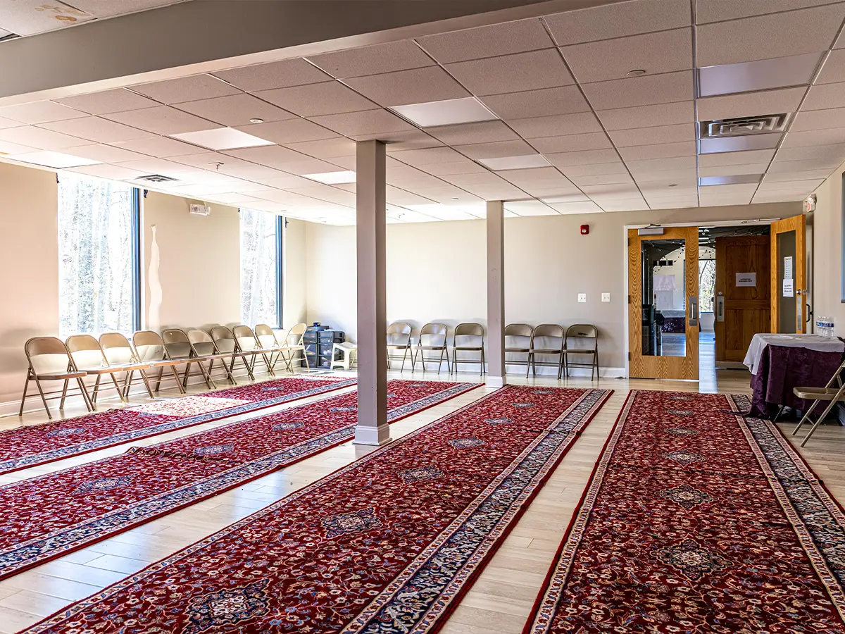 Community space in a mosque with red carpets and seating, used for lectures and special gatherings.