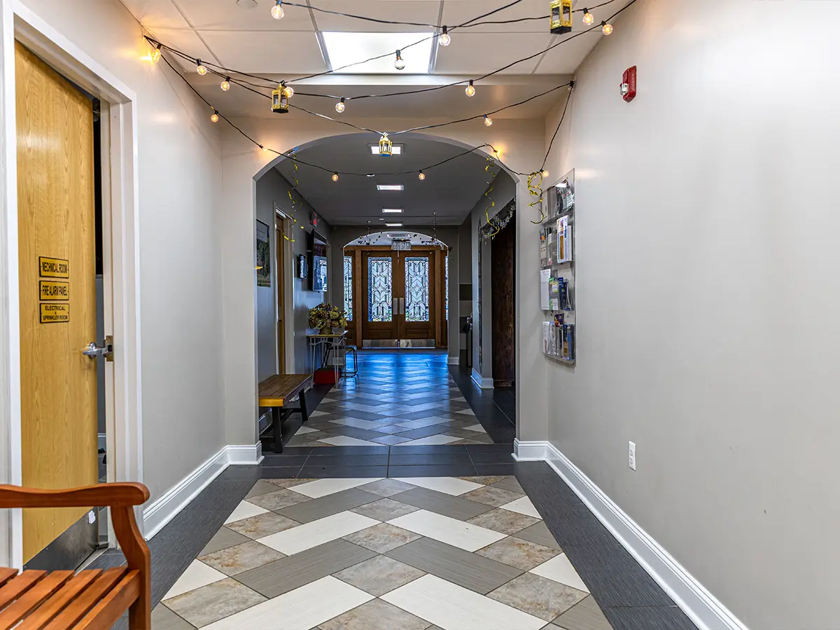 Bright and welcoming hallway with geometric tile flooring and festive string lights, leading to the mosque entrance.